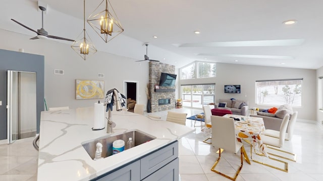 kitchen featuring a fireplace, sink, hanging light fixtures, ceiling fan, and light stone counters