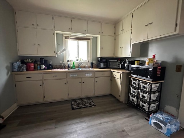 kitchen with a toaster, stainless steel microwave, white cabinets, a sink, and light wood-style flooring