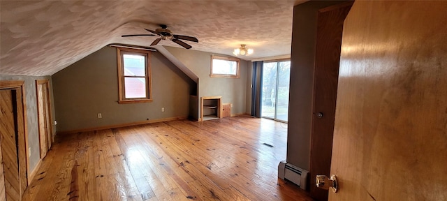 additional living space with vaulted ceiling, ceiling fan, light wood-type flooring, a textured ceiling, and a baseboard radiator