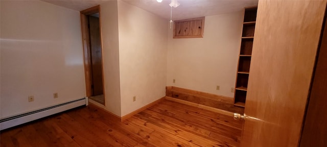 unfurnished room featuring wood-type flooring and a baseboard heating unit