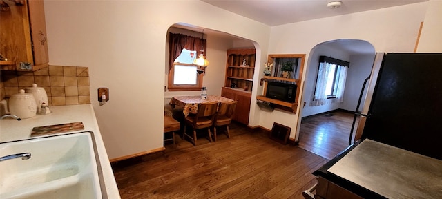 kitchen featuring decorative backsplash, dark wood-type flooring, hanging light fixtures, stainless steel refrigerator, and plenty of natural light