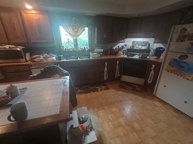 kitchen featuring white fridge, tile countertops, light parquet flooring, range, and sink