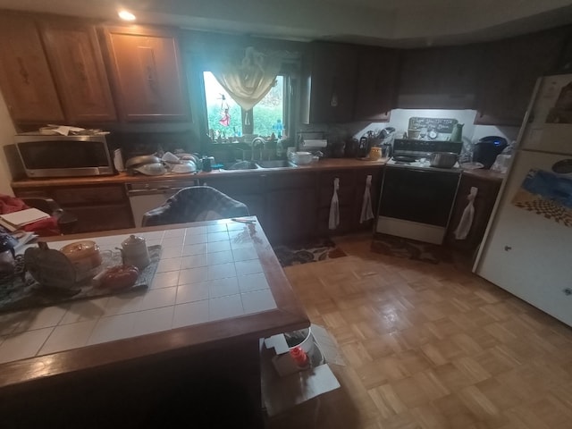 kitchen with light parquet flooring, sink, tile countertops, and range