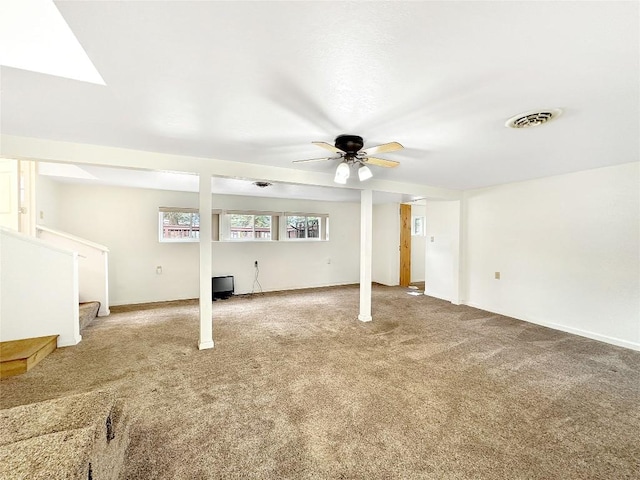 below grade area featuring carpet, stairway, visible vents, a ceiling fan, and baseboards