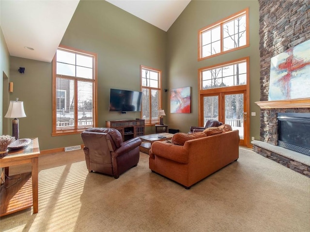 living room with a stone fireplace, light colored carpet, and a towering ceiling