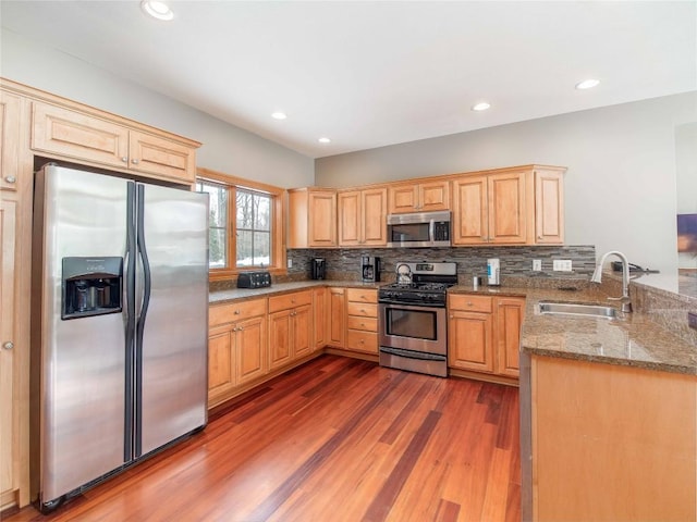 kitchen featuring sink, hardwood / wood-style flooring, stainless steel appliances, light stone counters, and kitchen peninsula