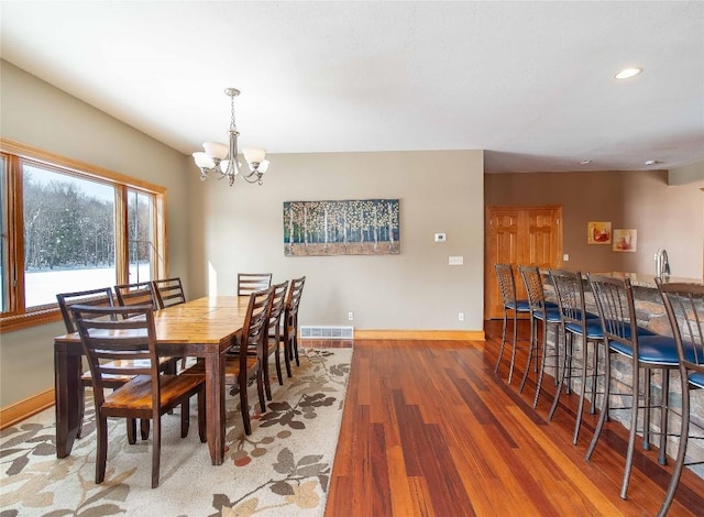 dining area with hardwood / wood-style flooring, bar area, and a chandelier