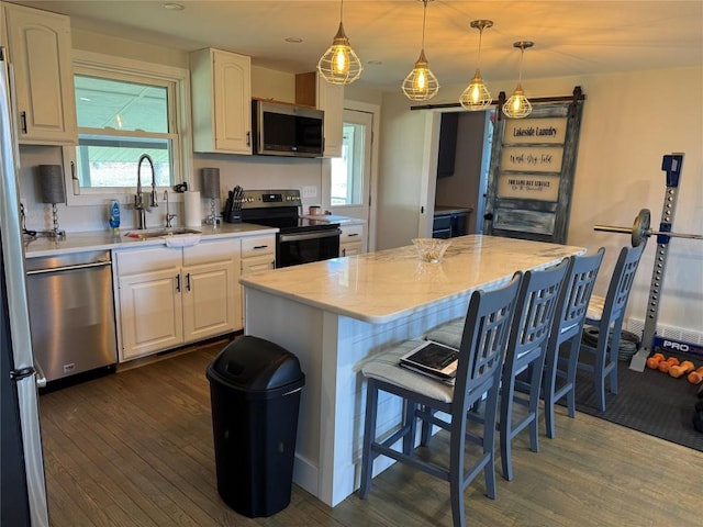 kitchen featuring dark wood-style flooring, a kitchen breakfast bar, white cabinets, appliances with stainless steel finishes, and a sink