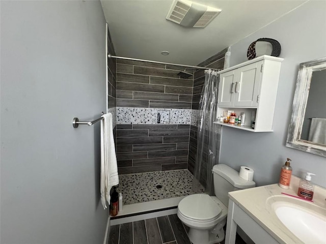 bathroom featuring vanity, toilet, visible vents, a tile shower, and wood finished floors