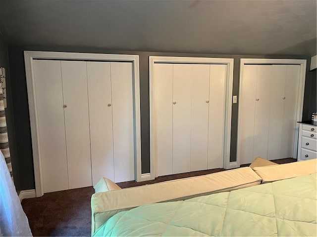 unfurnished bedroom with dark colored carpet and two closets