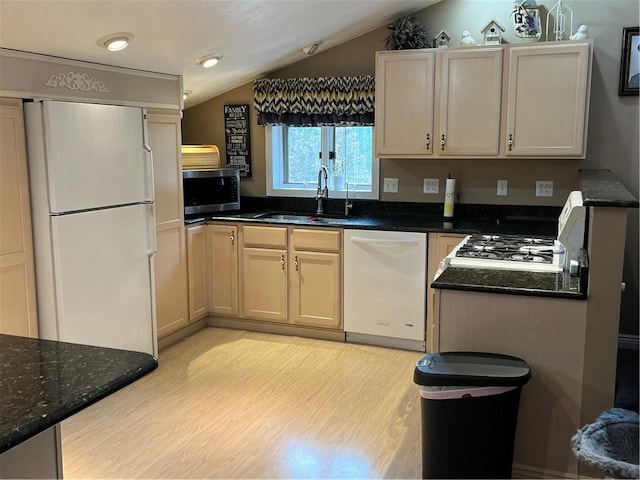 kitchen with appliances with stainless steel finishes, vaulted ceiling, sink, light hardwood / wood-style flooring, and dark stone countertops