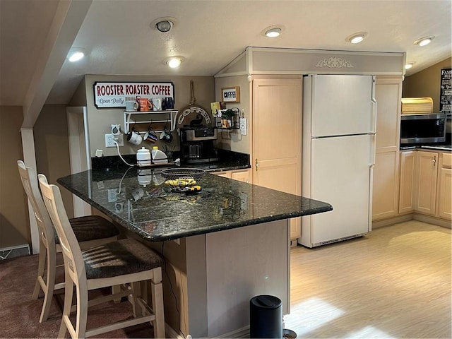 kitchen featuring white refrigerator, a kitchen bar, lofted ceiling, and dark stone counters