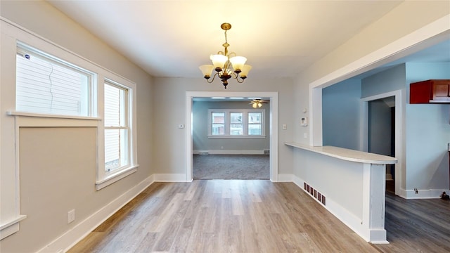 unfurnished dining area featuring ceiling fan with notable chandelier, a healthy amount of sunlight, and light wood-type flooring