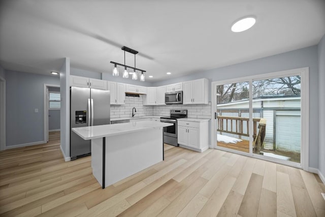 kitchen featuring a kitchen island, appliances with stainless steel finishes, decorative light fixtures, sink, and white cabinets