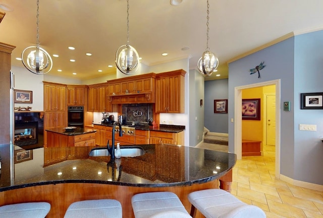 kitchen with sink, dark stone countertops, pendant lighting, a breakfast bar, and a center island with sink