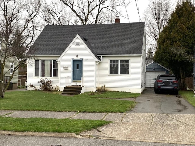 new england style home featuring an outdoor structure, a garage, a front yard, roof with shingles, and a chimney