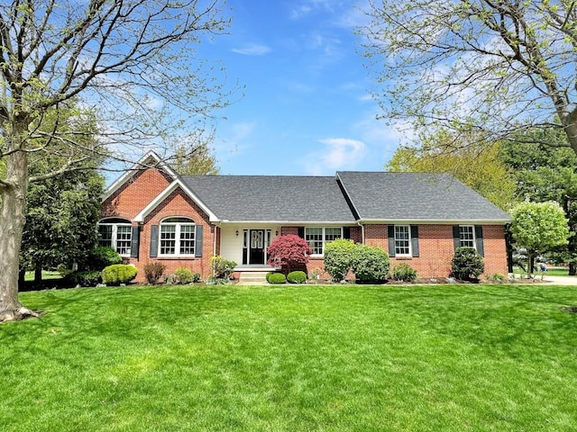 ranch-style home featuring brick siding, roof with shingles, and a front yard