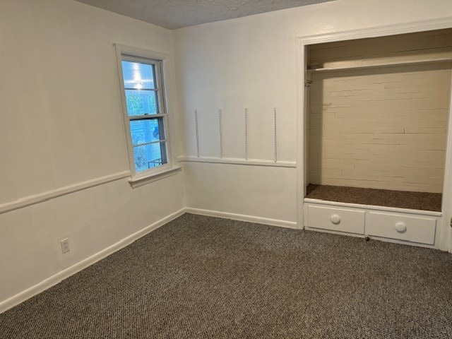 unfurnished bedroom with a closet, a textured ceiling, and dark colored carpet