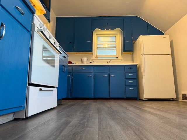 kitchen with sink, white appliances, blue cabinets, and vaulted ceiling