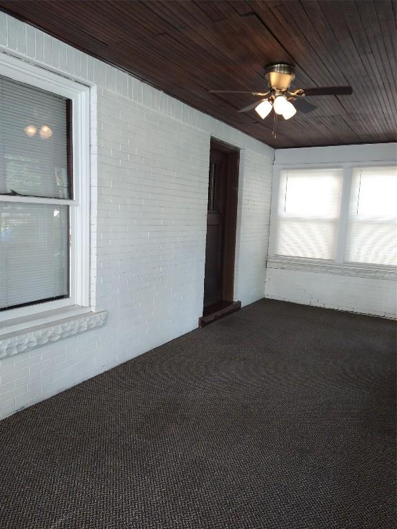 spare room with ceiling fan, dark carpet, wooden ceiling, and brick wall