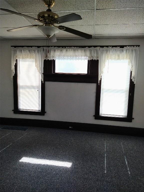 carpeted spare room featuring ceiling fan, a drop ceiling, and plenty of natural light