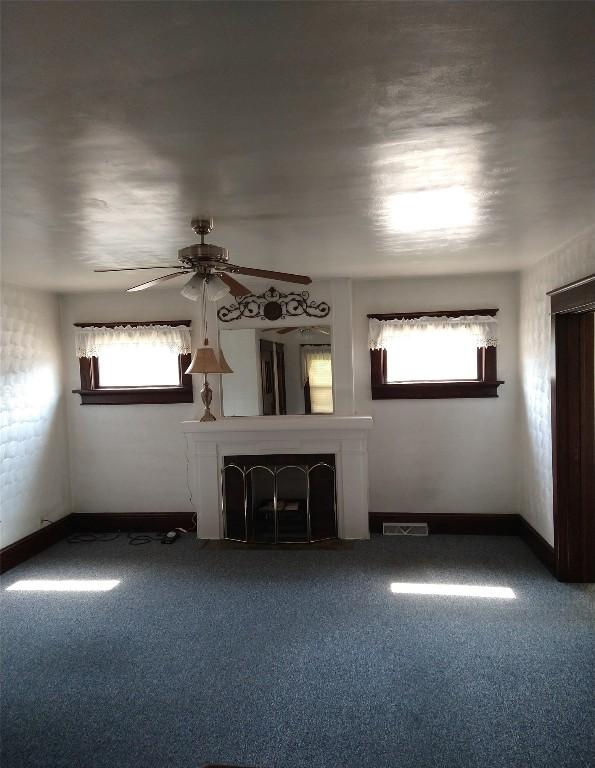 unfurnished living room featuring carpet flooring, ceiling fan, and a wealth of natural light