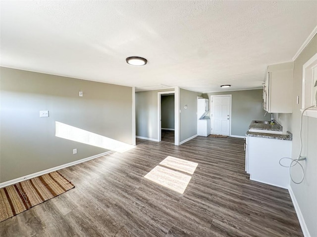 unfurnished living room with dark wood-style floors, a textured ceiling, a sink, and baseboards