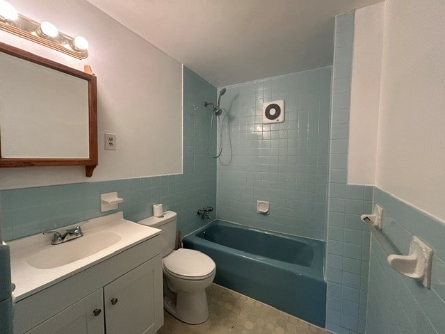 bathroom featuring vanity, toilet, tile walls, wainscoting, and washtub / shower combination