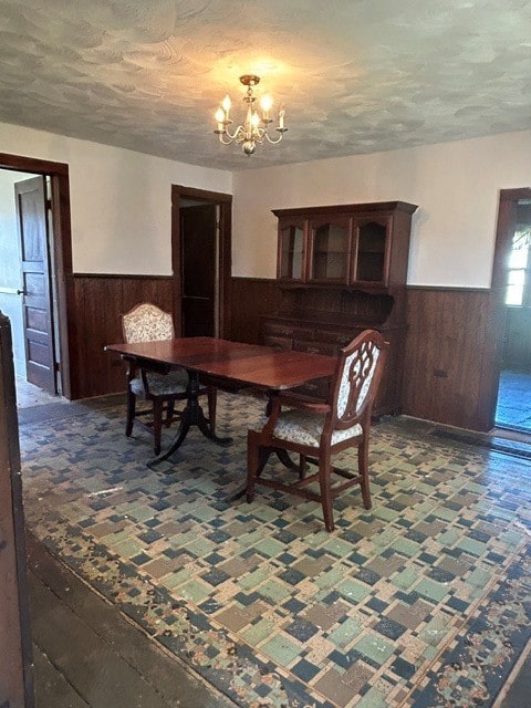dining area featuring a textured ceiling, a notable chandelier, a wainscoted wall, and wood walls