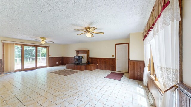 8410 Windsor Beach Ct, Erie, PA 16511 - unfurnished living room featuring wainscoting, wooden walls, a wood stove, a ceiling fan, and a textured ceiling