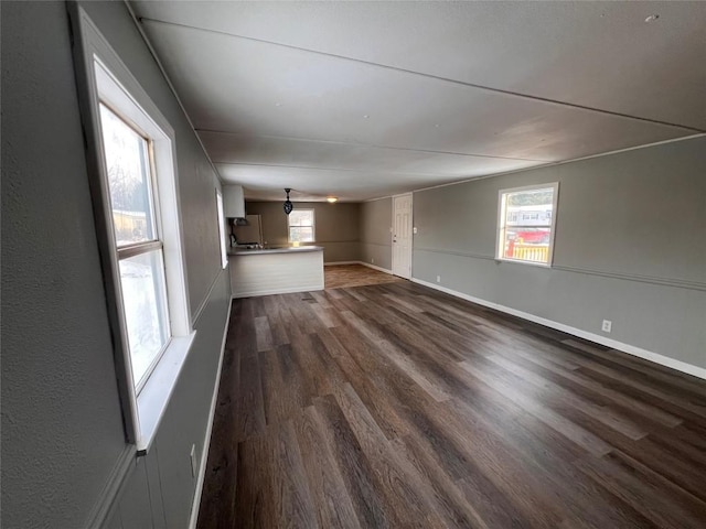 unfurnished living room featuring dark wood-style floors, baseboards, and a healthy amount of sunlight