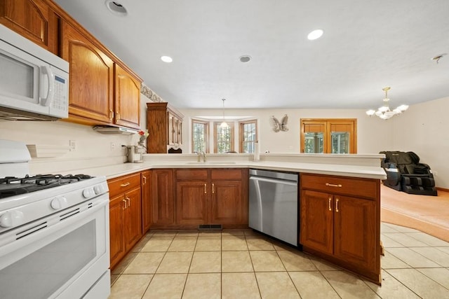 kitchen with light tile patterned floors, kitchen peninsula, decorative light fixtures, white appliances, and sink