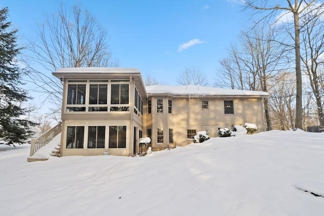 snow covered rear of property featuring a sunroom