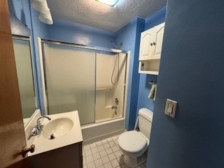 full bathroom featuring combined bath / shower with glass door, vanity, a textured ceiling, tile patterned floors, and toilet