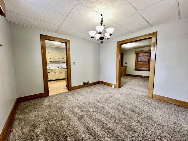 carpeted spare room with a paneled ceiling and a notable chandelier