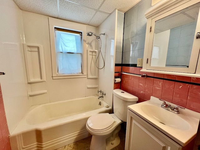 full bathroom with a drop ceiling, vanity, shower / tub combination, toilet, and tile walls