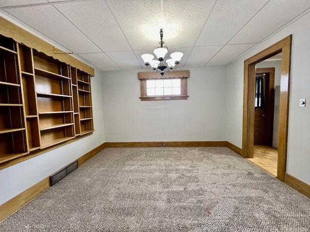 spare room with a paneled ceiling, carpet floors, and a notable chandelier