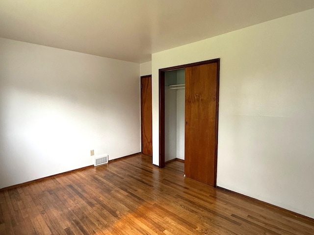 unfurnished bedroom featuring baseboards, visible vents, wood finished floors, and a closet