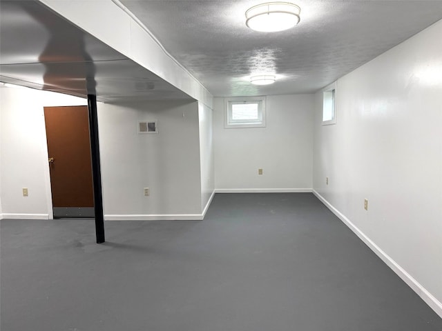 below grade area with visible vents, a textured ceiling, and baseboards