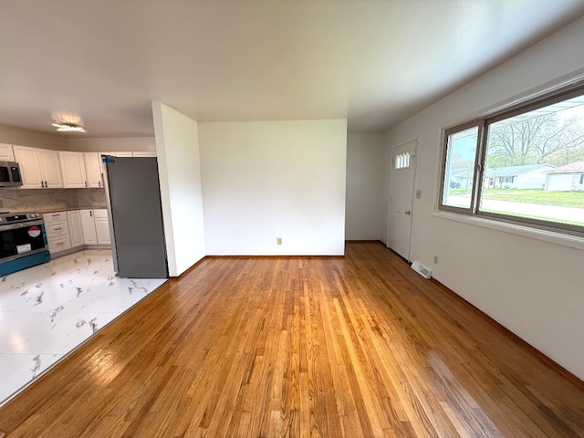 unfurnished living room with baseboards, light wood-style flooring, and visible vents