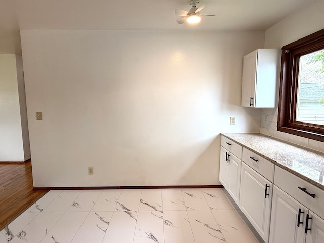 kitchen featuring light stone counters, marble finish floor, a ceiling fan, baseboards, and white cabinetry