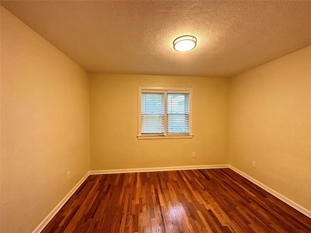 spare room featuring a textured ceiling, dark wood-style flooring, and baseboards