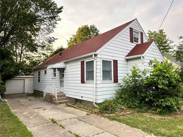 bungalow-style house featuring a garage, concrete driveway, a shingled roof, and an outdoor structure