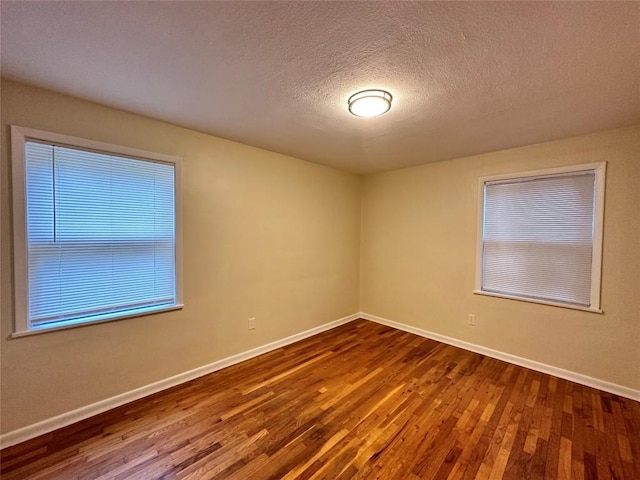 spare room with dark wood-style floors, a textured ceiling, and baseboards