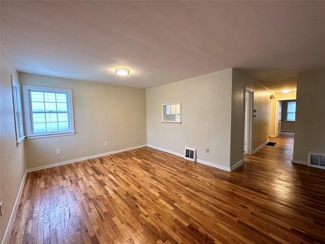 unfurnished room featuring baseboards, visible vents, and wood finished floors