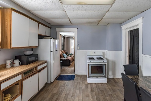 946 W 17th St, Erie, PA 16502 - kitchen with white appliances, a paneled ceiling, wood finished floors, a wainscoted wall, and white cabinetry
