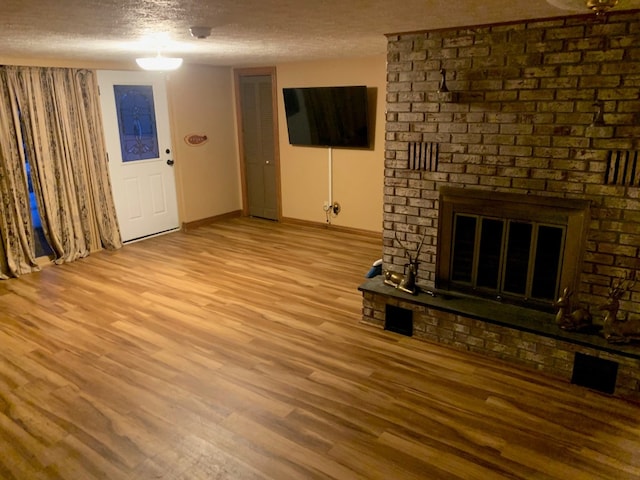 unfurnished living room featuring light wood-type flooring, a textured ceiling, and a brick fireplace