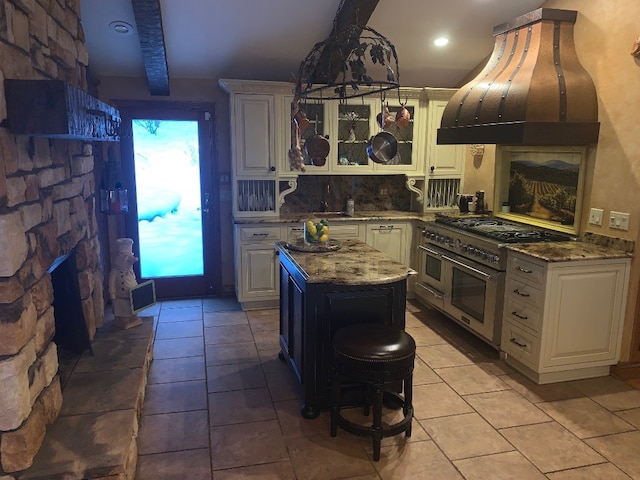 kitchen with dark stone counters, double oven range, beamed ceiling, a center island, and range hood