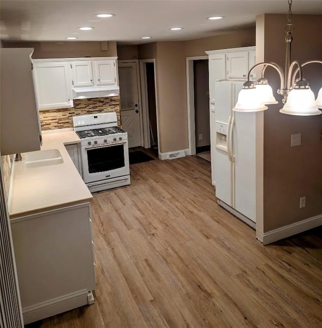 kitchen with white appliances, white cabinets, decorative backsplash, hanging light fixtures, and light hardwood / wood-style flooring