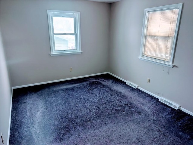 empty room featuring dark carpet, visible vents, and baseboards